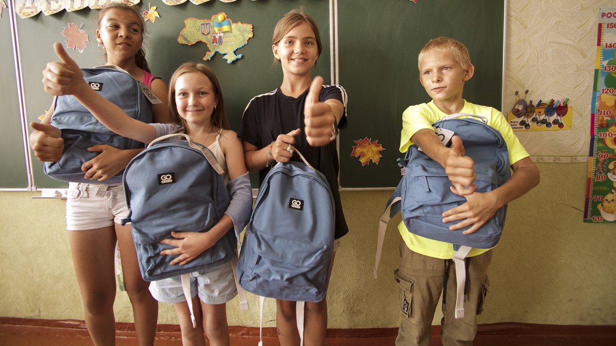 Človek v ohrození rozdává vnitřně vysídleným ukrajinským dětem školní batohy s pomůckami.